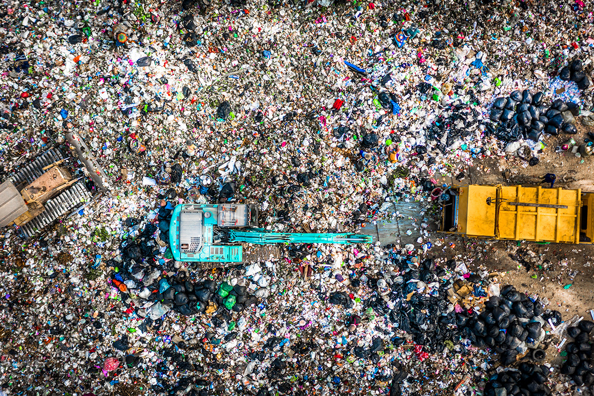 Aerial drone view of an active municipal solid waste landfill with garbage trucks unloading into massive piles of mixed refuse — PFAS-containing products buried in landfills leach into liquid that migrates to groundwater