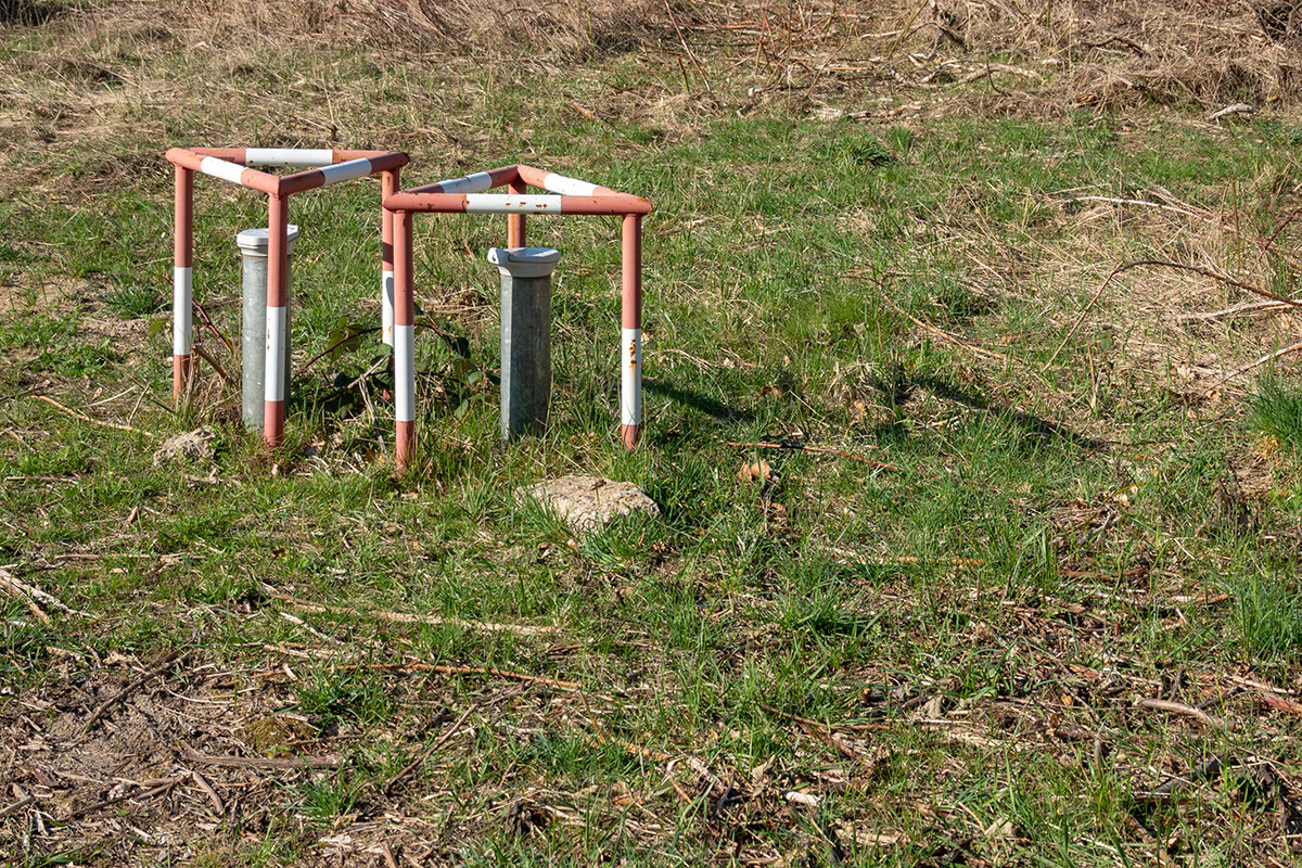 Groundwater monitoring well heads with protective steel frames installed in a field — environmental monitoring wells are used to detect PFAS migration from landfills into surrounding groundwater