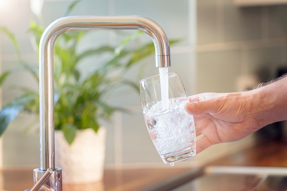 Person filling glass with clean filtered drinking water from kitchen tap after PFAS treatment system installation