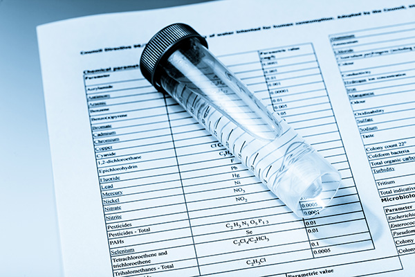 Water quality laboratory testing results showing PFAS contamination analysis with chemical test vials and comprehensive contaminant screening form