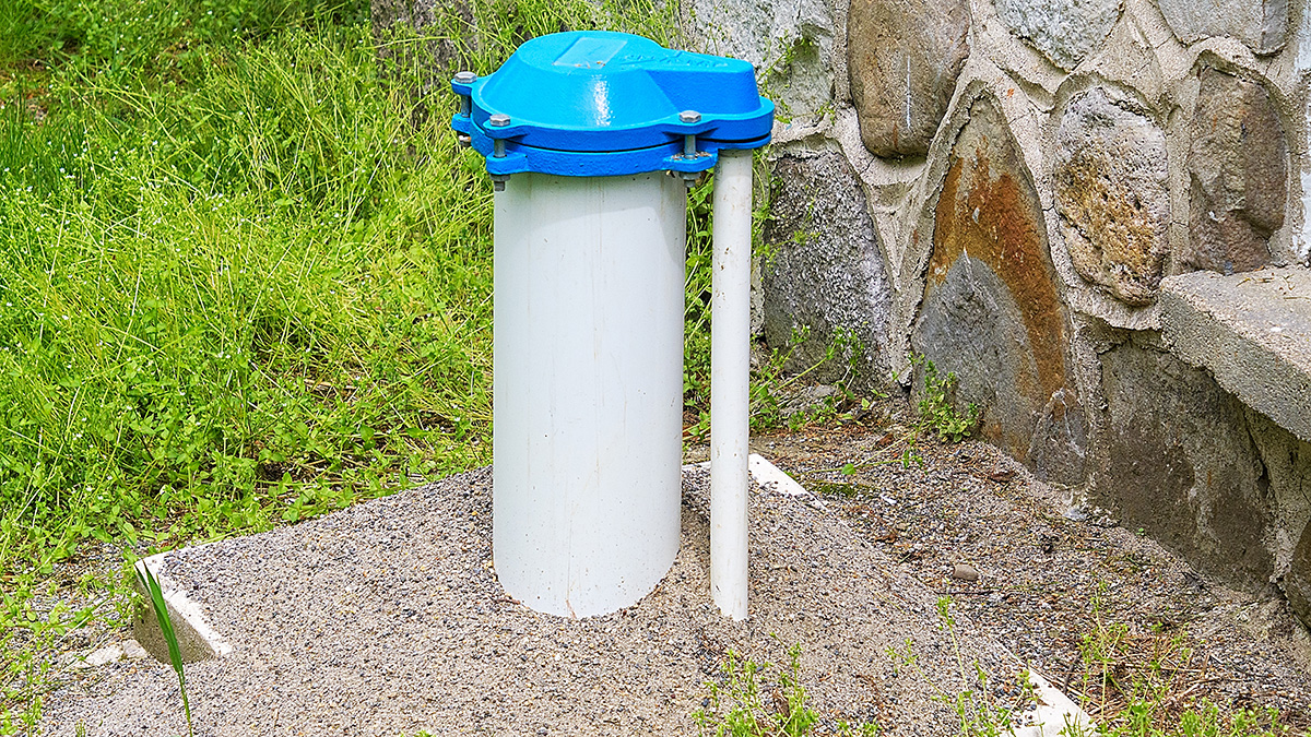 White casing and blue bolted cap of a private home water well beside a stone wall. EPA does not regulate private wells, and PFAS testing is the responsibility of the well owner.