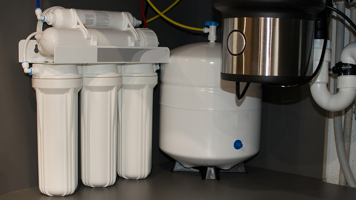 Under-sink reverse osmosis system with multi-stage filter cartridges and a storage tank installed in a home kitchen cabinet, one of the point-of-use options used to reduce PFAS in private well water.