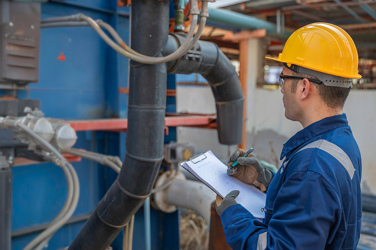 Water treatment engineer with clipboard inspecting industrial piping and filtration equipment at a remediation facility